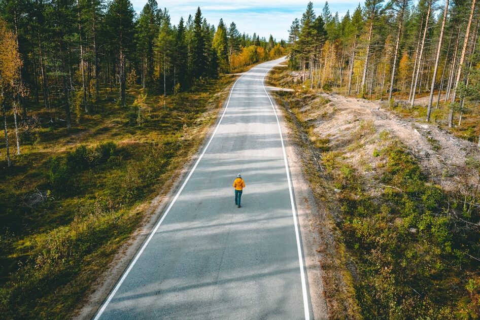 Ihminen seisoo yksin keskellä autiota autotietä.