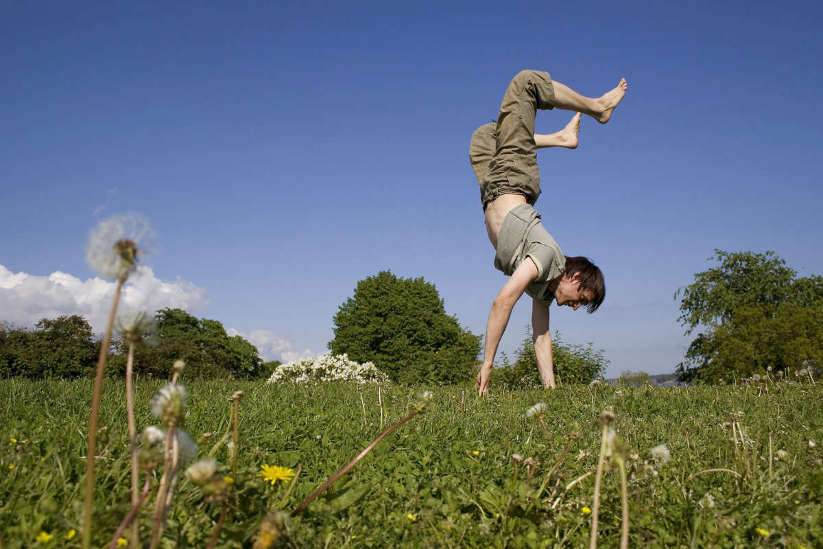 A young man is doing a handstand on the grass.