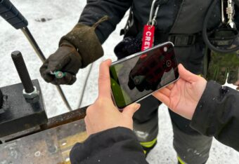 Suojakäsineisiin pukeutunut henkilö pitelee vioittunutta paristoa ja toinen henkilö kuvaa puhelimella.